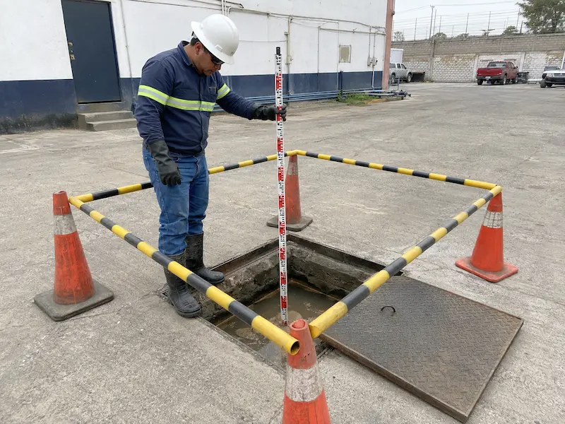 Técnico abre un registro de drenaje y mide la profundidad de sedimento dentro del predio